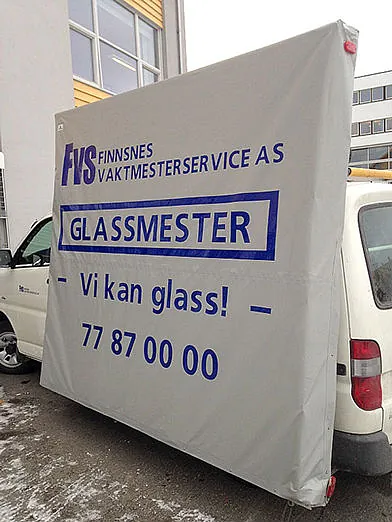 Hvit varebil med høy last tildekket av grå presenning med blå reklame.